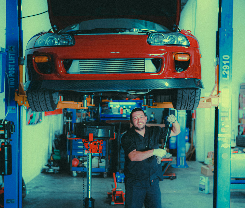 Mechanic working beneath a red sports car on a workshop lift